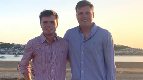 Family handout Jack and his older brother Ben O'Sullivan standing side by side on a beach at sunset. They are both wearing Ralph Lauren collared shirts and smiling at the camera, with their arms around each other.