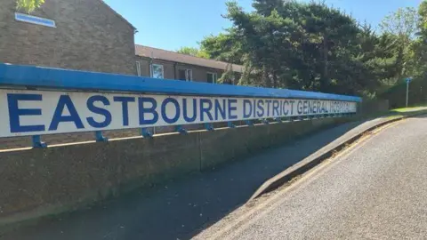 A blue sign outside a hospital that reads Eastbourne District General Hospital. 