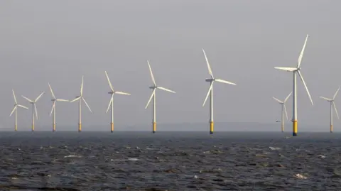 A line of wind turbines in the sea. The blades and tower are white with yellow at the base