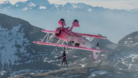 46 Aviation A person stands on a plane's wings as it flies upsidedown over mountains 