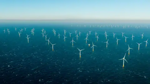 Charlotte Webb/National Grid A drone image of a wind farm located in the middle of a sea. Wind turbines are placed in long rows next to each other.