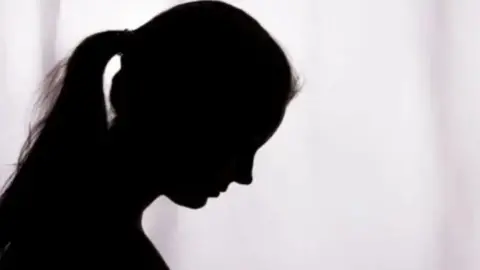 A generic image of a woman in silhouette looking down. The woman has her hair up in a ponytail. 