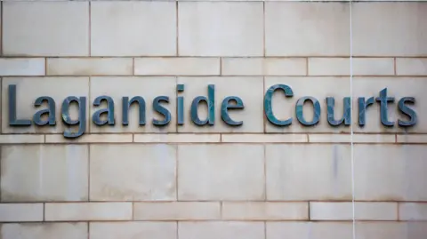 Blue/grey sign on a cream brick wall, reading - Laganside Courts