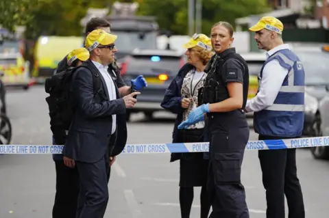 PA Media A police woman is shown along with security staff near a police cordon across a street