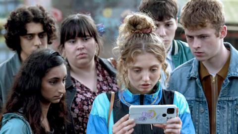 A scene from Red Rose, with teenagers looking at a mobile phone