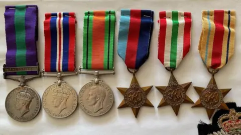 Gloucestershire Police Three circular, silver medals with colourful ribbons, laid on a white cloth alongside three bronze medals shaped like stars with colourful ribbons.