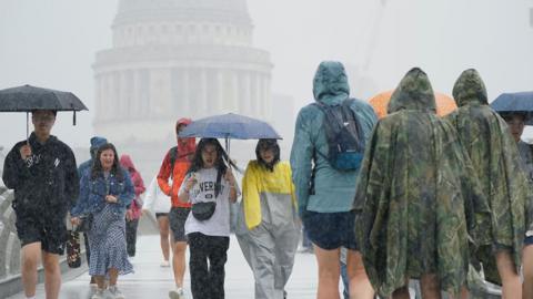 Several people are caught in heavy rain as they cross The Millennium Bridge over the river Thames in London. 