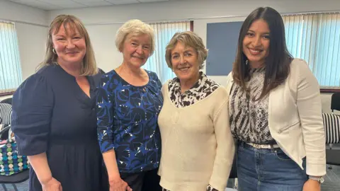 Four women stand together smiling at the camera