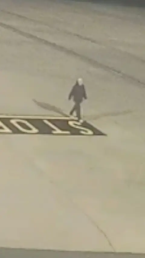 A man in a black jacket walking on an airport apron 