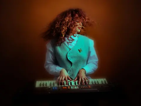 Ellen Beth Abdi playing a keyboard while wearing a turquoise waistcoa