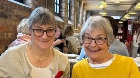 Supplied Jo Hollick, with short hair and glasses, sat next to her mum, Ann Mallett, at a dinner table.