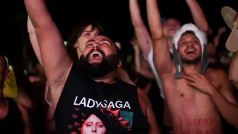 Concert goers with arms in the air and mouths open, smiling 