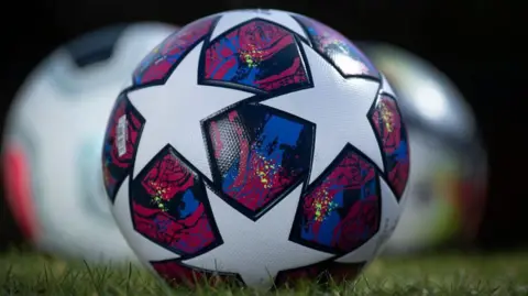 Getty Images A close up of a professional football. It is emblazoned with white stars on a purple, black and blue swirly background. 