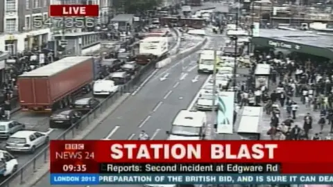 A photo of BBC News 24 TV channel at 0935 on the day of the blast. The caption says "station blast" and underneath "Reports: second incident at Edgware Rd". A large crowd can be seen outside Kings Cross overground station with traffic backed up on the opposite side of the road.