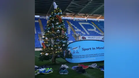 Sport in Mind A Christmas tree decorated with trainers on the pitch in front of the stand at Reading FC's stadium