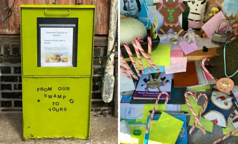 Wil Keiper Photo of the outside of the Skrek Box, made from an old newspaper box painted green, next to various Shrek items inside the box