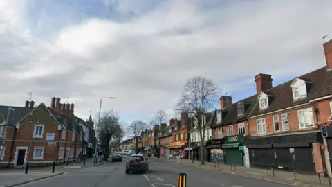 Stores on one side of a street in Leicester with cloudy skies above