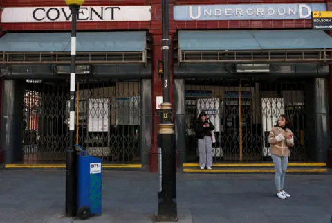 Reuters Women on phones stand outside Covent Garden Tube station with shutters closed