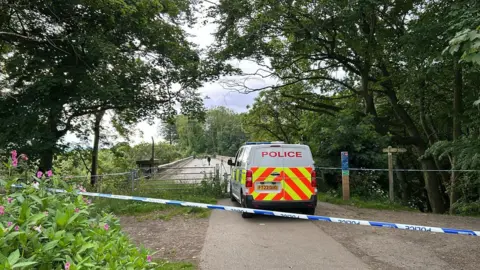 Jacob Tomlinson/BBC Police van in front of bridge with police tape behind it