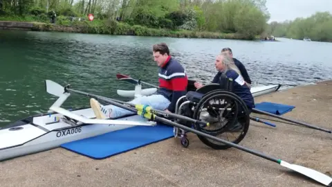 Ben Pritchard is using the hoist, with assistance to get into a rowing boat on the River Thames.