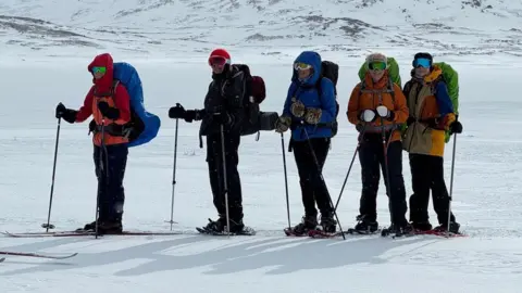Five women in full ski gear and on skis with poles in snowy conditions