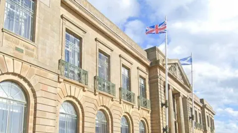 A large sandstone council building, with Union Jack and Saltire flags flying above it