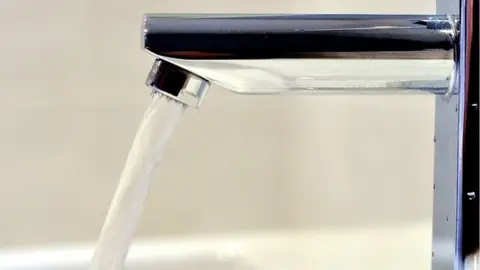 PA An open stainless steel tap with water rushing out of the spout and a white background