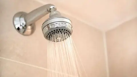 Getty Images Silver shower head with water coming out in cream tiled bathroom.