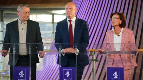 PA Media Three people - Anthony Slaughter, Dan Thomas, Eluned Morgan, stood next to each other in front of lecterns 