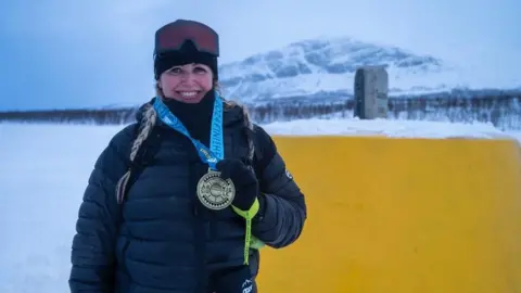 Anya in thermals holding a medal for finishing an event in the arctic circle.