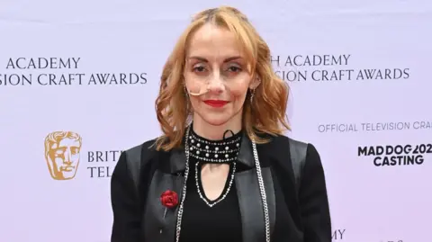 Getty Images Natalie Amber attends the Bafta awards in a sparkly black outfit. She wears red lipstick and has blonde hair.