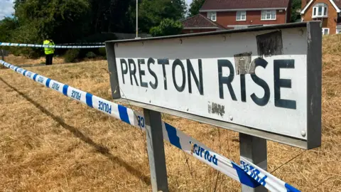 Police tape tied around the Preston Rise street name sign with an officer in high viz uniform standing nearby