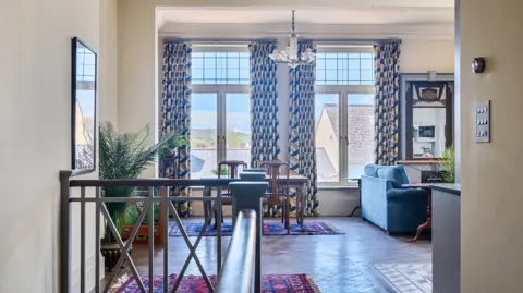 Symonds and Sampson Interior of one of the apartments decorated in an Art Deco style with wooden stair bannisters, ornate tinted mirror, patterned curtains and wooden furniture.