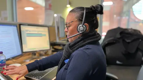 A call handler on the phone at a call centre in Station Street, Nottingham. She is wearing a headset and sitting in front of two computer screens