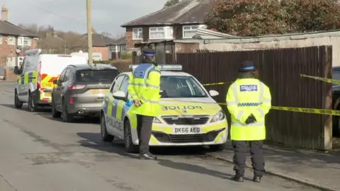 Two community support officers in yellow high-vis coats on guard near a residential garage