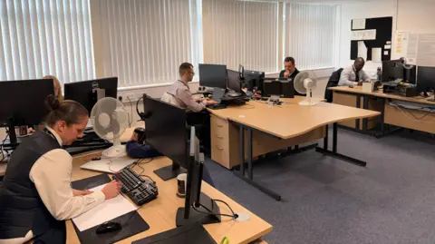 Five members of staff at the DSCC are sitting at wooden desks in an office space