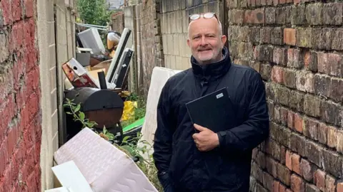 Councillor Peter Harvey stood in an alleyway full of rubbish