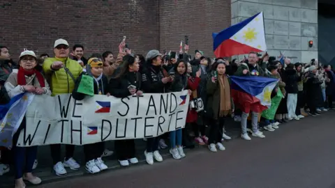 Getty Images Supporters of the Philippines' former president Rodrigo Duterte gather outside The Hauge Penitentiary Institution, holding the country's flag and a white banner that says "We stand with Duterte"