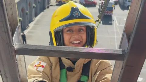 BBC A smiling woman in a firefighter's uniform climbing a ladder