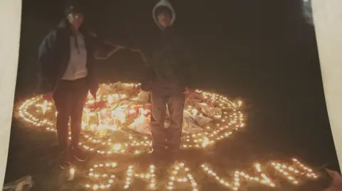 Family  Maneshwary and Suresh standing next to candles spelling Shawn's name