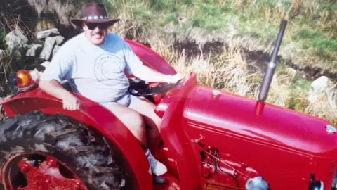 Dave Harrison Dave Harrison riding a red tractor parked on a green field. He smiles wearing sunglasses, a dark brown cowboy hat, t-shirt and shorts.