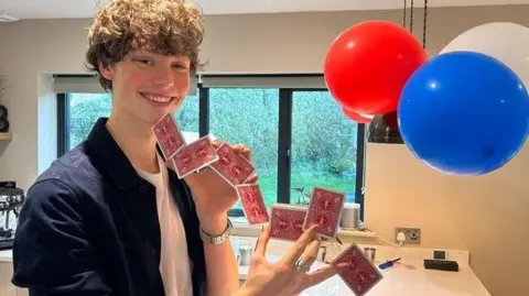 BBC Rafferty in his kitchen smiling and holding playing cards between his fingers