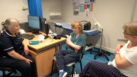 A nurse, a young patient, and her mother, all sitting in a medical office.