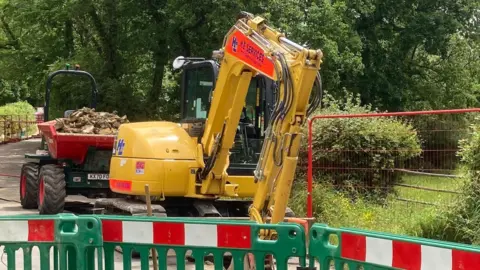 A road closed with a digger behind fences digging up the road