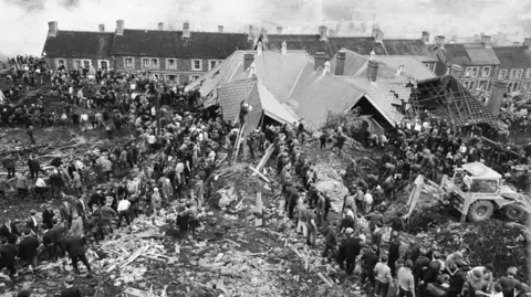 Getty Images Black and white image of lines of villagers and emergency services helping to free trapped children and adults