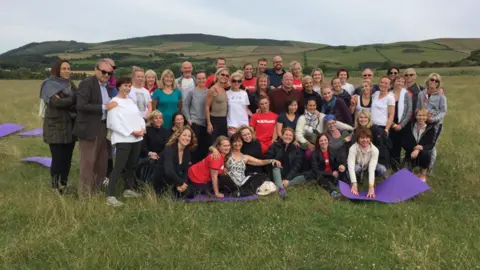 Knockaloe.im A group of people stand and sit in the field of Knockaloe in 2016 after the conference. 