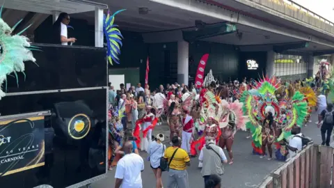 Colourfully dressed masqueraders gather beside a sound system truck during the launch event of Notting Hill Carnival.