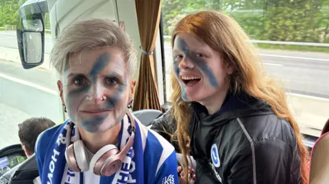 Two people with blue and white face paint on. They are sitting on a coach.