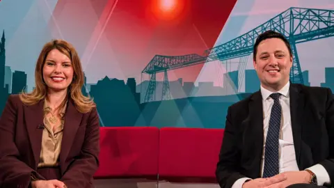 BBC Kim McGuinness and Ben Houchen sat smiling together on the red sofa on BBC Politics North. She has long blonde hair and he has short black hair.