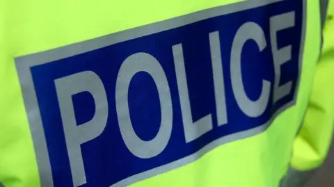 BBC The back of a fluorescent police jacket with the word "police" in silver letters on a blue background.